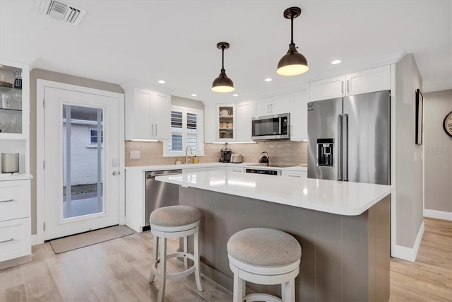 kitchen with a center island, pendant lighting, stainless steel appliances, light hardwood / wood-style floors, and white cabinets