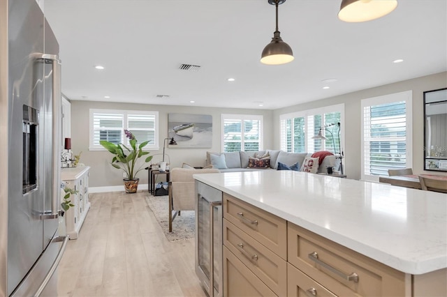 kitchen with high end refrigerator, a center island, light wood-type flooring, pendant lighting, and a healthy amount of sunlight