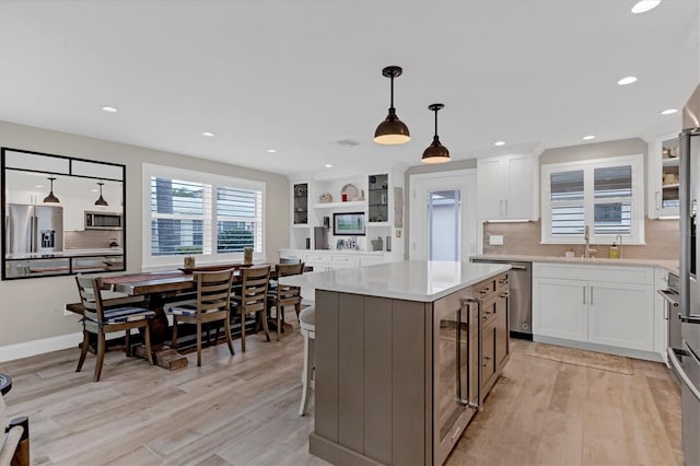 kitchen featuring white cabinets, hanging light fixtures, a center island, light hardwood / wood-style floors, and stainless steel appliances