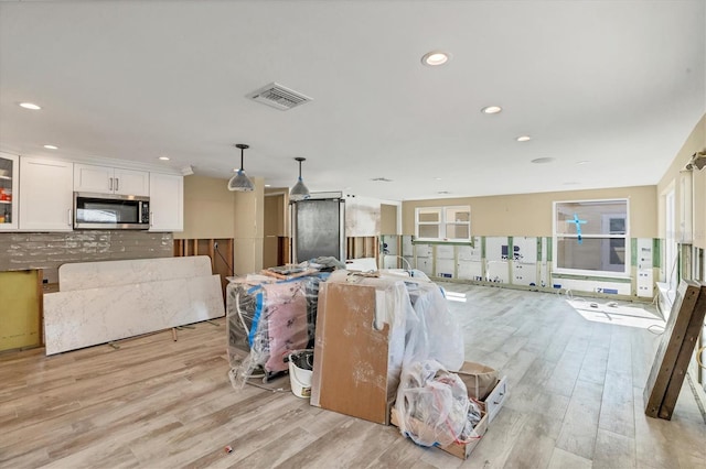 interior space featuring white cabinetry, decorative light fixtures, light hardwood / wood-style flooring, and tasteful backsplash