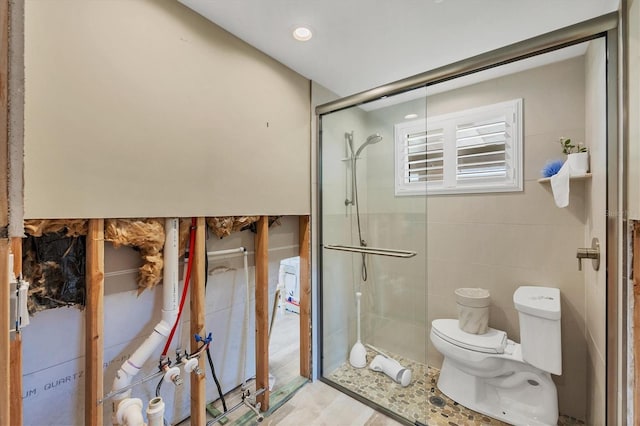 bathroom featuring tile walls, a shower with door, and toilet