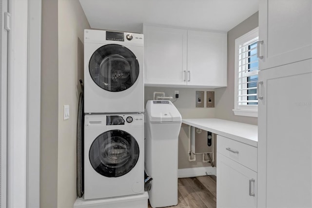 clothes washing area featuring light wood-type flooring, cabinets, and stacked washing maching and dryer