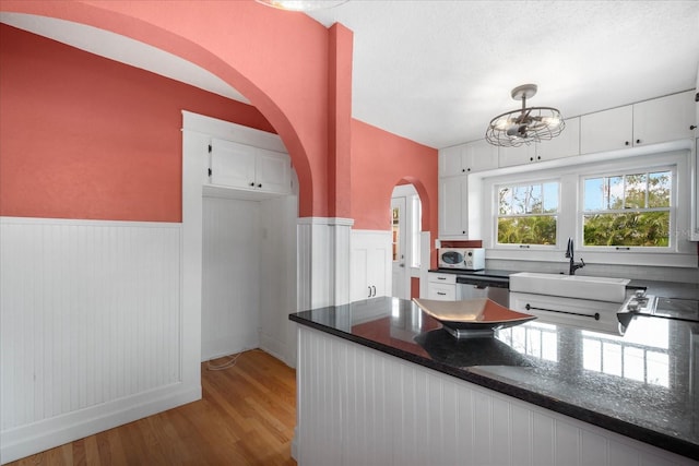 kitchen featuring white cabinetry, stainless steel dishwasher, dark stone counters, and light wood-type flooring