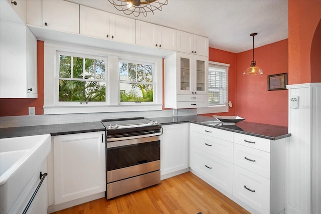 kitchen with dark countertops, light wood finished floors, glass insert cabinets, stainless steel electric range oven, and white cabinetry