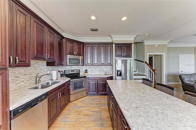 kitchen featuring appliances with stainless steel finishes, tasteful backsplash, sink, ornamental molding, and light wood-type flooring