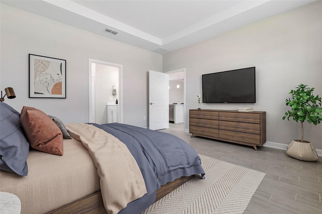 bedroom featuring a tray ceiling, ensuite bath, and light hardwood / wood-style floors