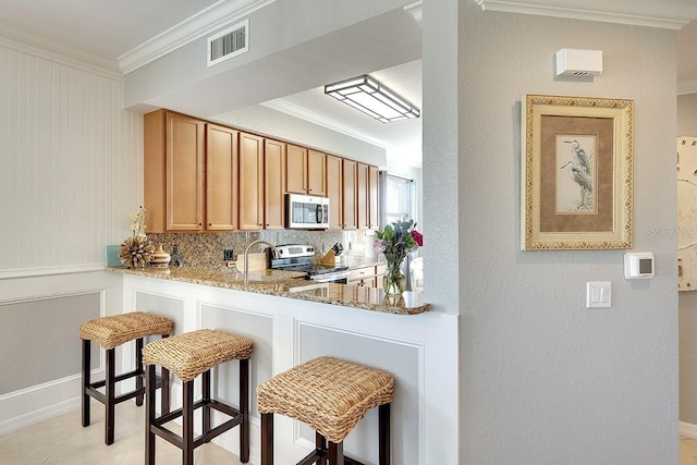 kitchen with crown molding, a breakfast bar area, light stone countertops, and appliances with stainless steel finishes