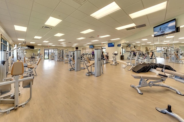 exercise room with a paneled ceiling and light wood-type flooring