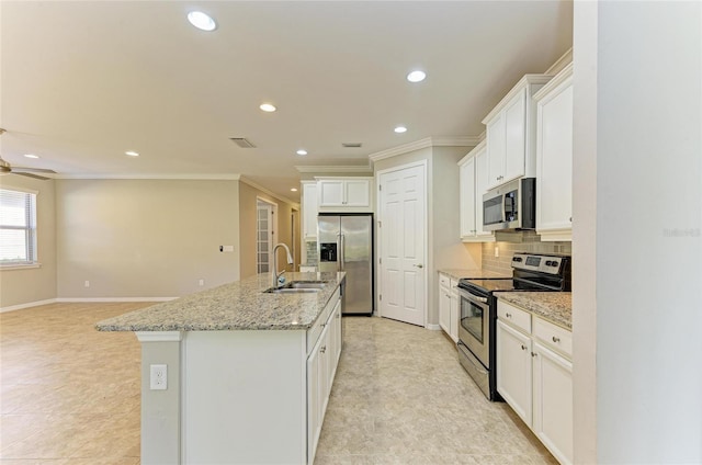 kitchen with backsplash, stainless steel appliances, light stone countertops, white cabinets, and a center island with sink