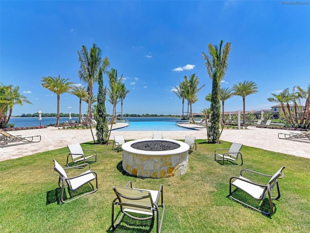 view of community featuring a patio, a water view, a lawn, and an outdoor fire pit