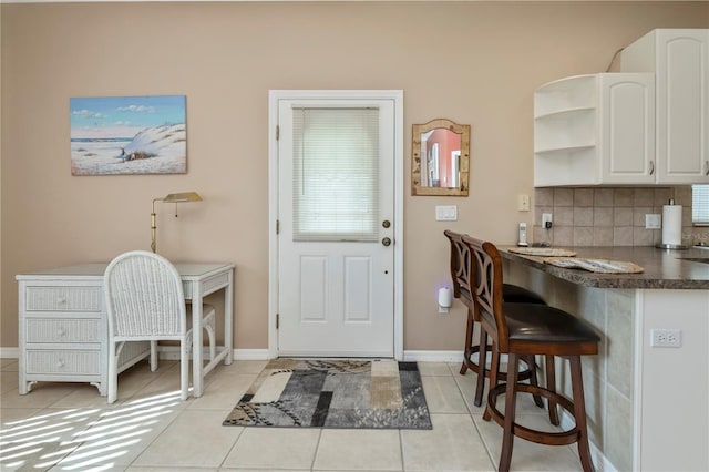 interior space featuring tasteful backsplash, a kitchen bar, light tile patterned flooring, and white cabinets