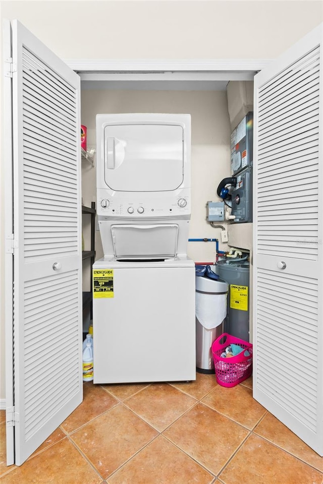 laundry area with stacked washer and dryer, light tile patterned floors, and water heater