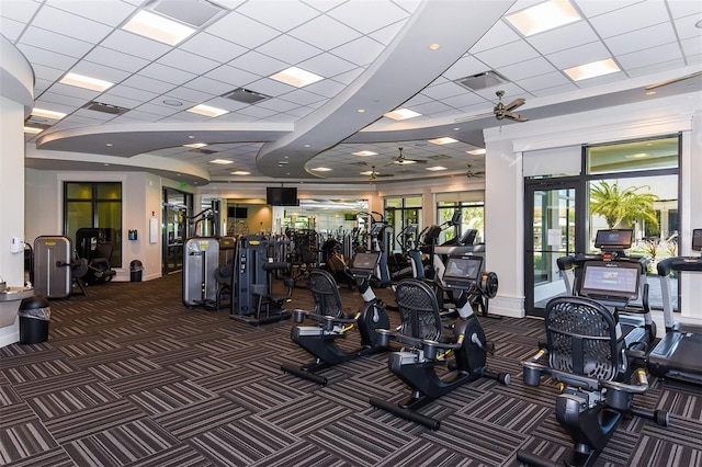 gym with ceiling fan, dark carpet, and a drop ceiling