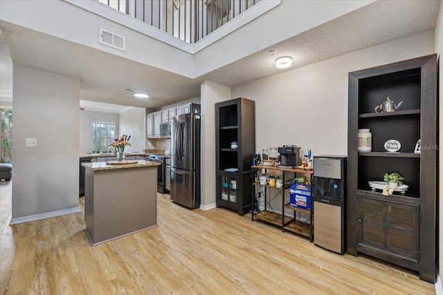 kitchen featuring stainless steel appliances, kitchen peninsula, a textured ceiling, and light wood-type flooring