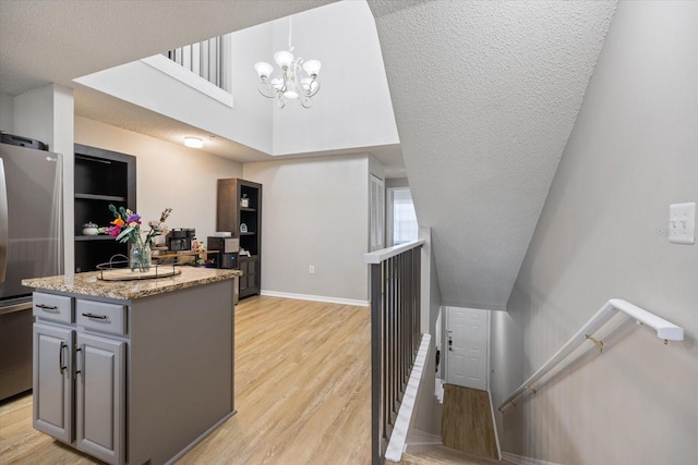 kitchen with gray cabinets, stainless steel fridge, hanging light fixtures, a center island, and light hardwood / wood-style floors