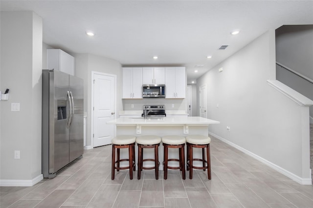 17136 Blowfish Dr, Nokomis, FL 34275 - kitchen featuring stainless steel appliances, light countertops, a kitchen island with sink, a kitchen bar, and white cabinetry