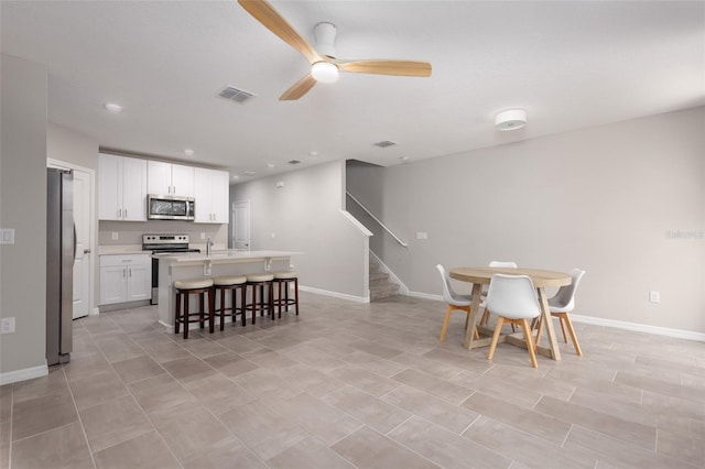 17136 Blowfish Dr, Nokomis, FL 34275 - kitchen with stainless steel appliances, ceiling fan, an island with sink, white cabinetry, and a breakfast bar