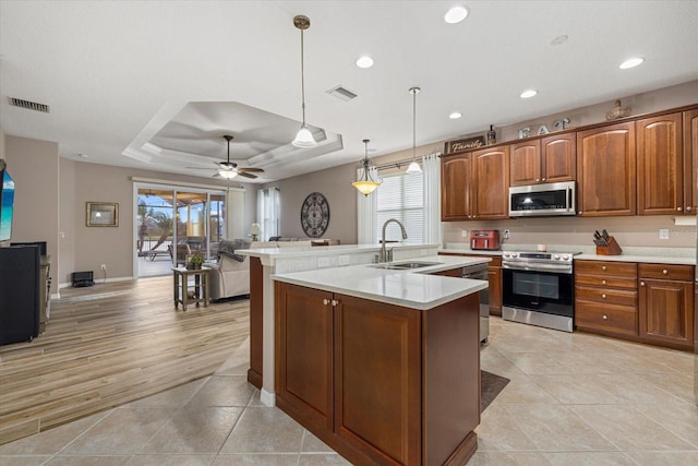 kitchen featuring sink, hanging light fixtures, a center island with sink, a tray ceiling, and stainless steel appliances