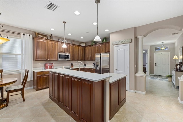 kitchen featuring stainless steel appliances, decorative light fixtures, an island with sink, and ornate columns