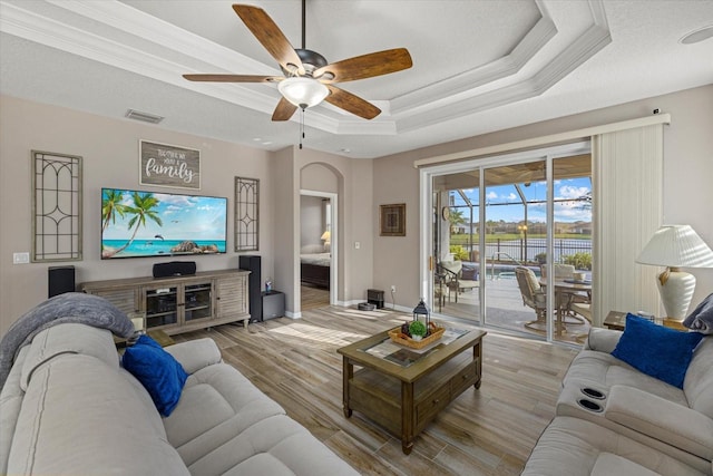 living room with ornamental molding, light hardwood / wood-style floors, a raised ceiling, and ceiling fan