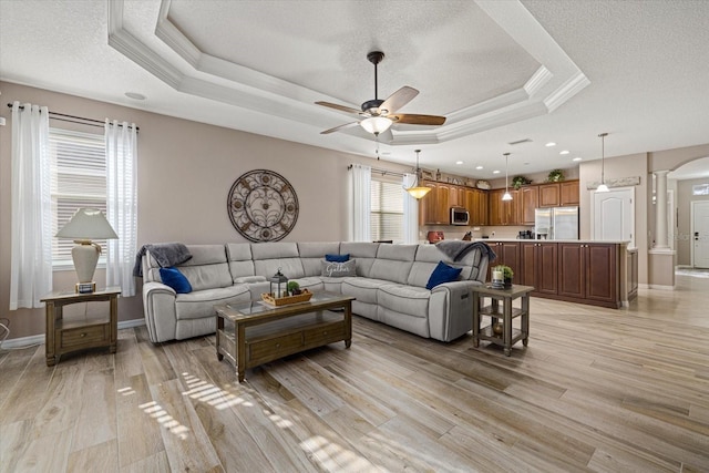 living room with light wood-type flooring, ceiling fan, a tray ceiling, crown molding, and a textured ceiling