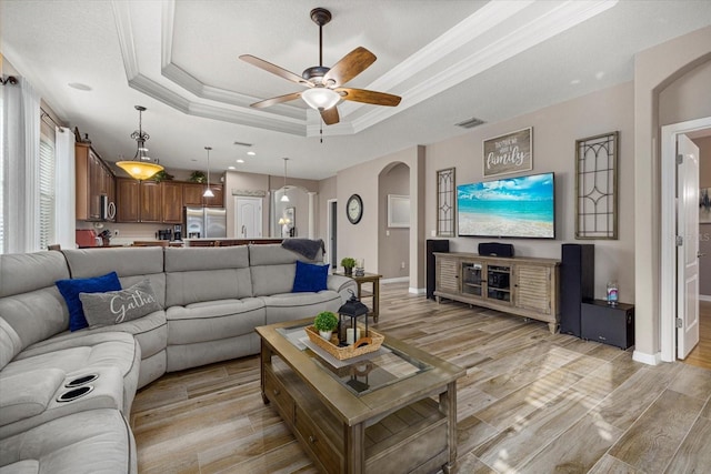 living room with ornamental molding, ceiling fan, light wood-type flooring, and a tray ceiling