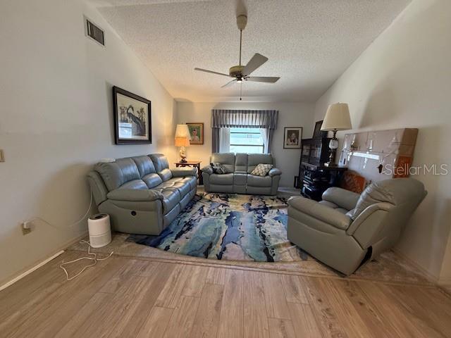 living room with a textured ceiling, ceiling fan, wood finished floors, visible vents, and vaulted ceiling