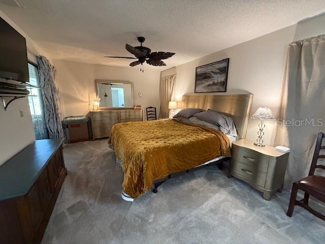 bedroom with a ceiling fan, dark carpet, and a textured ceiling