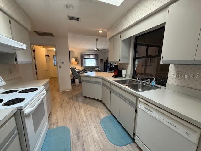 kitchen featuring white appliances, visible vents, open floor plan, light countertops, and a sink