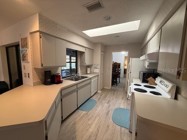 kitchen with a skylight, light countertops, visible vents, white appliances, and wallpapered walls