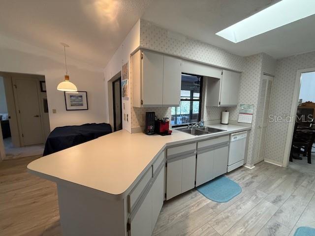 kitchen featuring a peninsula, a sink, light countertops, dishwasher, and wallpapered walls