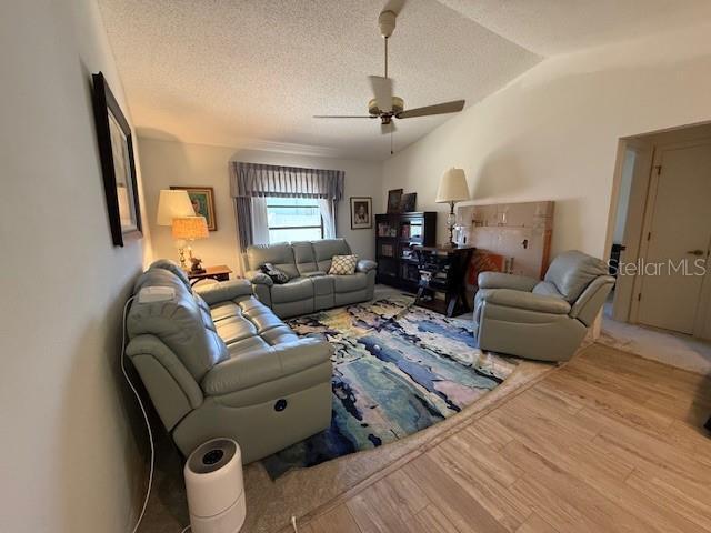 living room featuring lofted ceiling, a textured ceiling, wood finished floors, and a ceiling fan