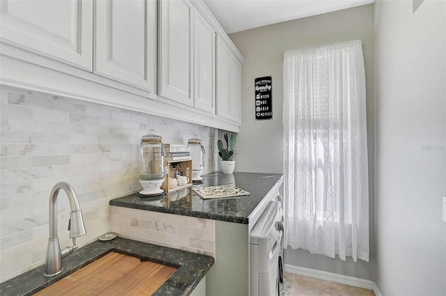 kitchen featuring white cabinetry, washer / dryer, sink, dark stone countertops, and decorative backsplash