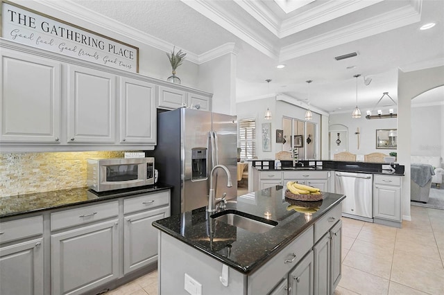 kitchen featuring sink, appliances with stainless steel finishes, kitchen peninsula, dark stone counters, and a kitchen island with sink