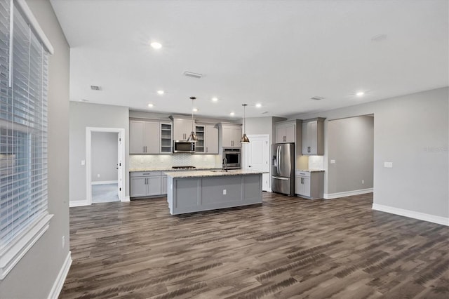 kitchen featuring an island with sink, appliances with stainless steel finishes, dark wood-type flooring, gray cabinetry, and pendant lighting