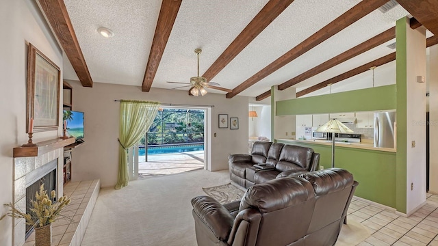 carpeted living room with ceiling fan, lofted ceiling with beams, a tile fireplace, and a textured ceiling