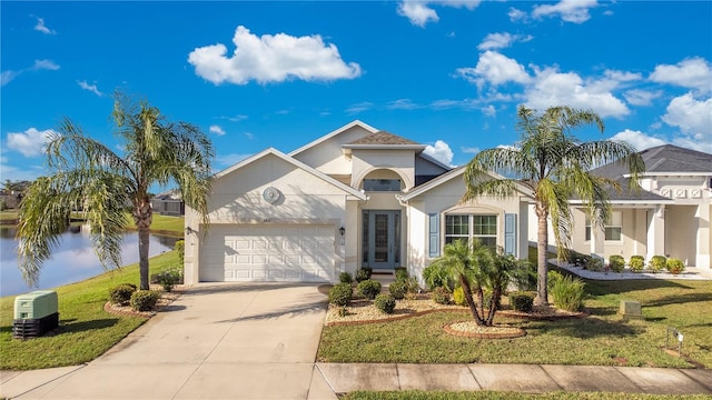 mediterranean / spanish house with a front yard, driveway, an attached garage, stucco siding, and a water view