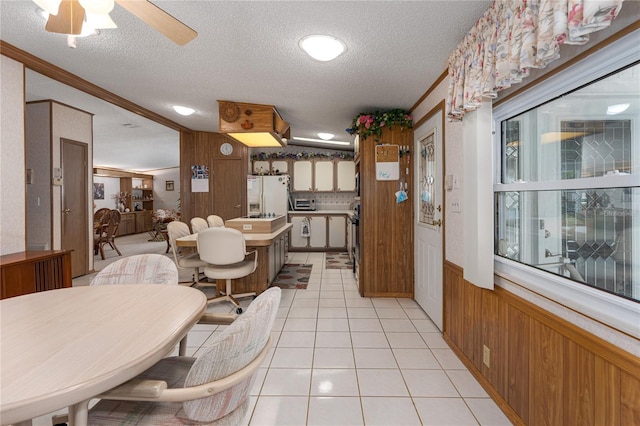 tiled dining space with ceiling fan, a textured ceiling, and wood walls