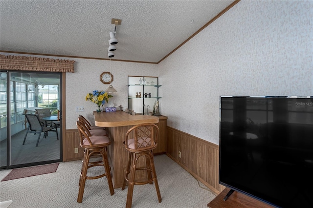 carpeted dining space with bar, vaulted ceiling, ornamental molding, and a textured ceiling