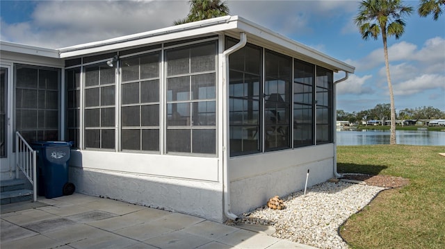 view of side of property with a water view, a sunroom, and a lawn