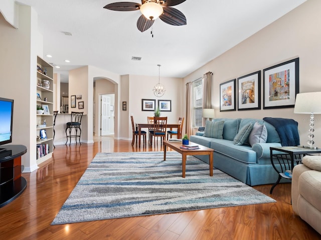 living area featuring built in features, arched walkways, visible vents, wood finished floors, and baseboards