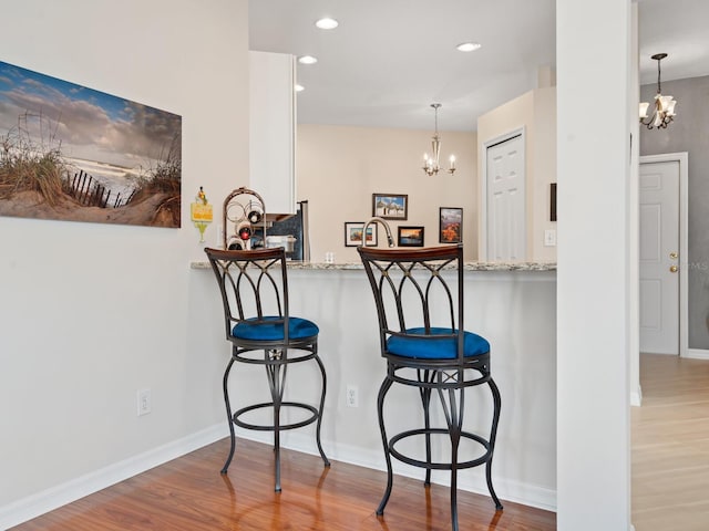 kitchen with a breakfast bar area, recessed lighting, wood finished floors, and a notable chandelier