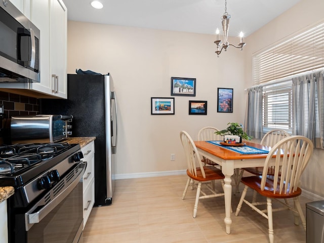 kitchen with white cabinets, range with gas stovetop, backsplash, stainless steel microwave, and an inviting chandelier