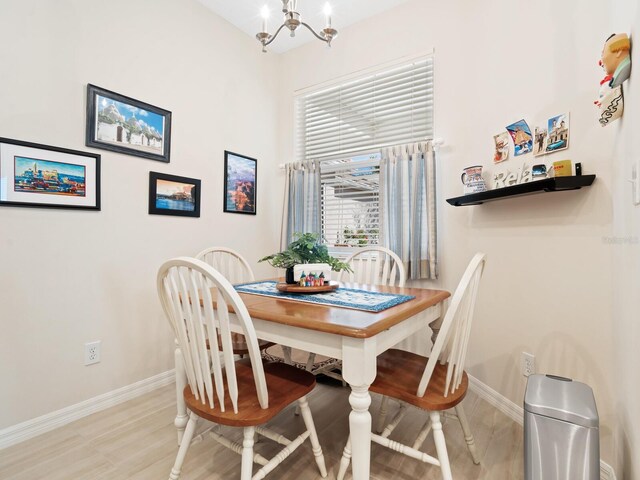 dining area with light wood-style floors, an inviting chandelier, a high ceiling, and baseboards