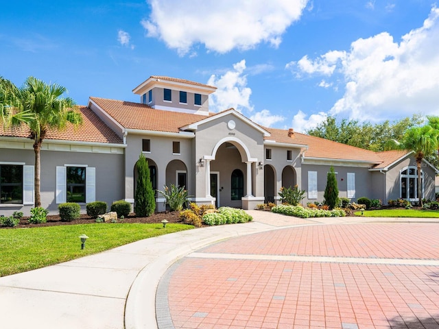 mediterranean / spanish home featuring a tile roof, a front lawn, and stucco siding