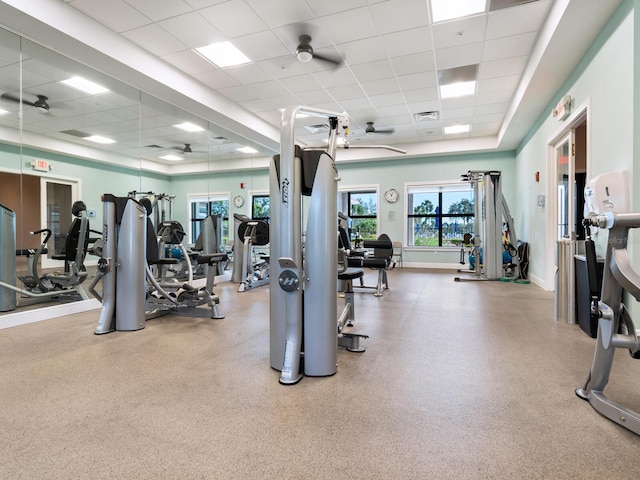 gym featuring a paneled ceiling, a raised ceiling, visible vents, ceiling fan, and baseboards