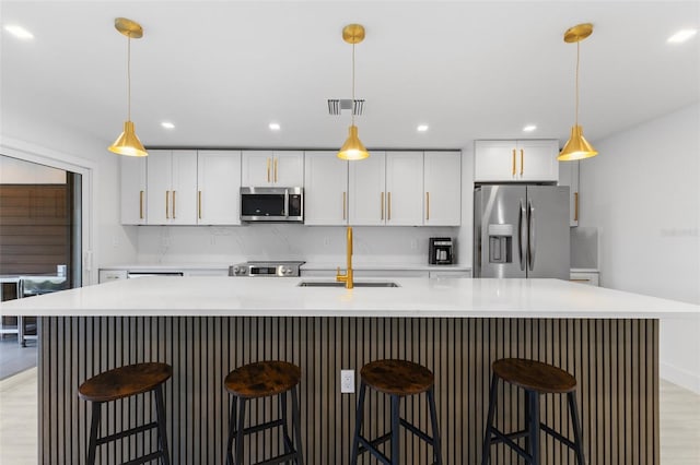 kitchen featuring a breakfast bar, sink, white cabinetry, a large island with sink, and appliances with stainless steel finishes