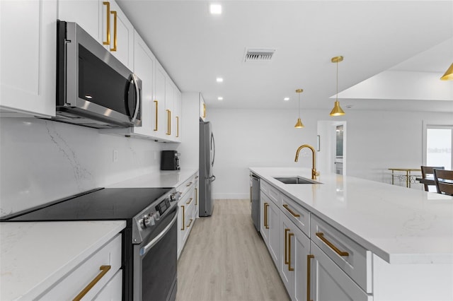 kitchen with pendant lighting, sink, white cabinets, stainless steel appliances, and a center island with sink