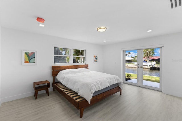 bedroom with french doors, a water view, access to exterior, and light hardwood / wood-style flooring