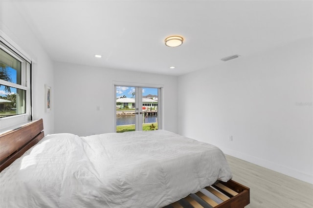 bedroom featuring access to exterior, light hardwood / wood-style floors, and a water view